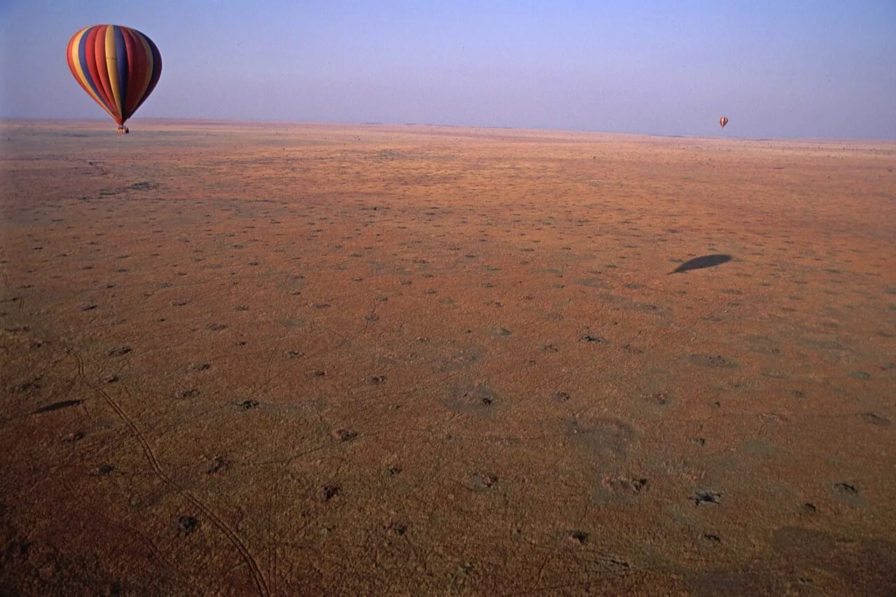 From a hot air balloon, you can see two other balloons, and the savannah littered with termite mounds. Taken on safari in Kenya.